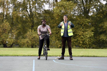 Woman on a bike in empty parking lot, man standing next to her 